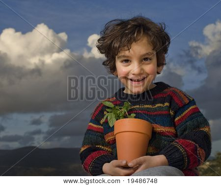 kleine jongen die een plant in een pot met wolken in de achtergrond