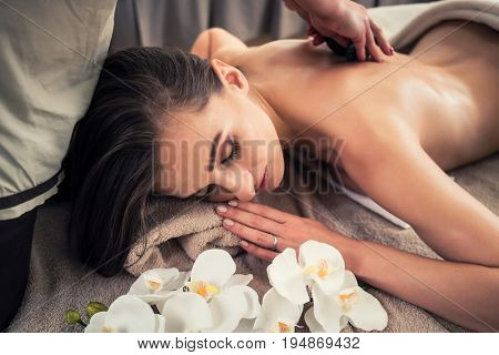 Young woman lying down while receiving hot stone massage at Asian spa and wellness center