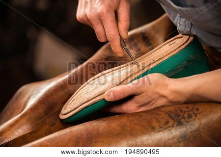 Cropped image of bootmaker sitting in workshop making shoes