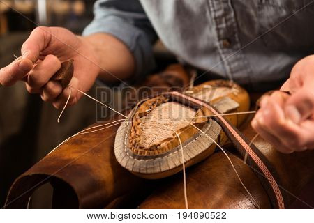 Cropped image of bootmaker sitting in workshop making shoes