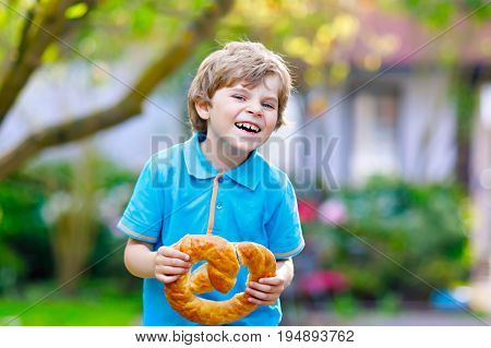 Adorable little kid boy eating huge big bavarian german pretzel. Happy blond child enjoying tasteful tratditional bread. Healthy food for happy kids.