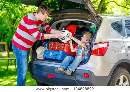 Adorable little kid boy sitting in car trunk just before leaving for summer vacation. Dad packing suitcases. Happy family going on long journey. happy family traveling. Summer travel.