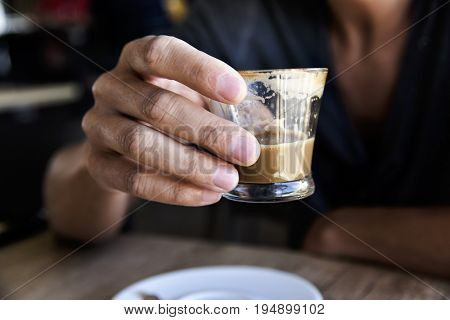 closeup of a young caucasian with a glass with caffe macchiato in his hand, sitting at a table in a coffeehouse