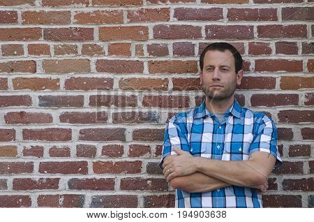 Portrait of an optimistic man leaning against a brick wall with his arms crossed thinking of what tomorrow will bring.