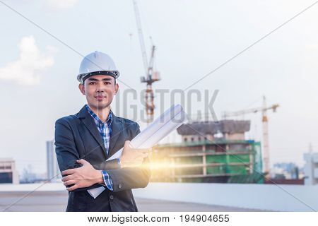 The architect wear white safety helmet and hold the blueprint with commitment on construction site with crane background