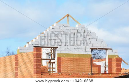 Attic construction with Mineral Wool Insulation House. Unfinished house with Building insulation. Attic Insulation with brick wall and wooden trusses and roof repair. Bricklaying Masonry Mansard Roof.