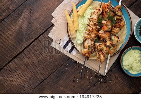 Barbecued chicken breast skewers with flat bread and avocado sauce on wooden table top view with copy space