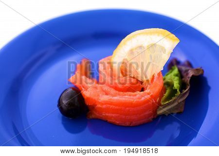 Slice of salmon with lemons and olives on a plate.