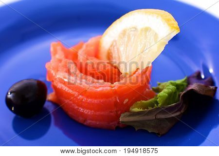 Slice of salmon with lemons and olives on a plate.
