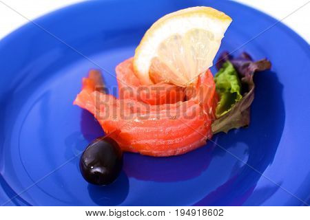 Slice of salmon with lemons and olives on a plate.