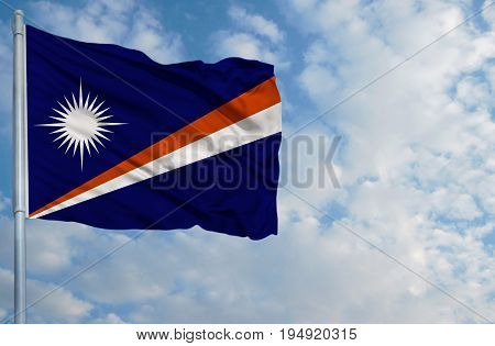 National flag of Marshall Islands on a flagpole in front of blue sky.