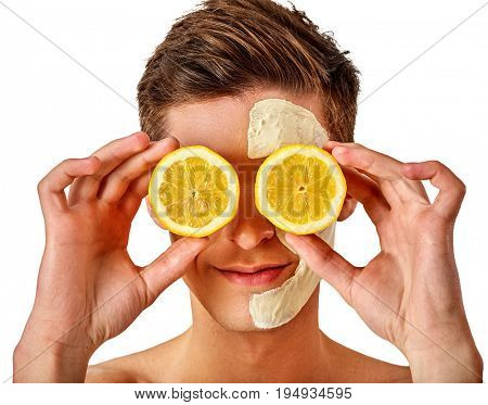 Facial mask from fresh fruits and clay for man concept. Face with treatment mud applied . Male holding lemon half for skin care procedure in salon. Lemon are main ingredient in cosmetic masks