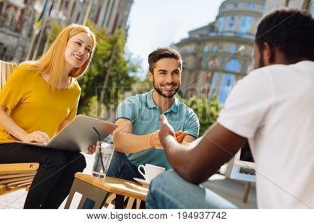 Another point of view. Innovative enthusiastic open minded man meeting his friends in a cafe and giving them the new concept he working while developing their common project