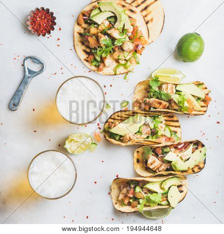 Healthy corn tortillas with grilled chicken, avocado, fresh salsa, limes, beer in glasses over light grey marble background, top view. Healthy food, gluten-free, allergy-friendly concept. Square crop