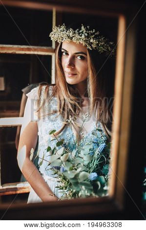the bride in a beautiful blue dress and a wreath of white flowers holding a bouquet of purple flowers and eucalyptus