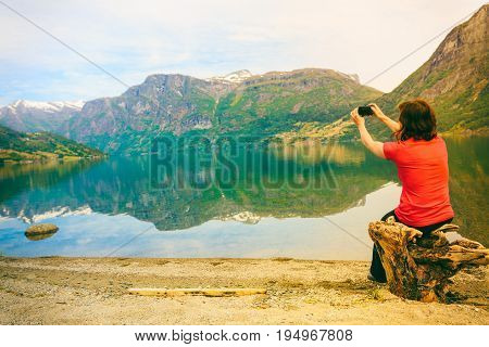 Tourism and travel. Woman tourist taking photo with camera enjoying mountains lake Oppstrynsvatnet view in Jostedalsbreen National Park Oppstryn (Stryn) Sogn og Fjordane county. Norway Scandinavia.