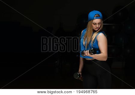 Fit sporty woman exercising with dumbbells and looking to her biceps muscles. Fitness female posing on black background. Fitness and healthy lifestyle concept.