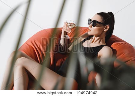 Gorgeous Young Woman In Sunglasses And Bodysuit Drinking Cocktail While Resting In Bean Bag Chair