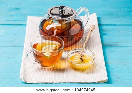 Glass cup of tea with lemon, glass teapot and honey on blue wooden table.