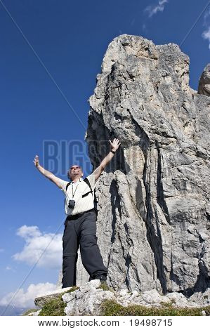 기쁨으로 그의 팔을 해제 하는 정상에 가까운 거 대 한 암석 앞에 서 있는 활성 수석 도보 여행자