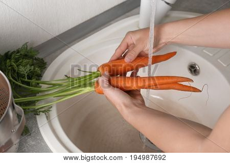 Woman washing fresh carrots in kitchen sink