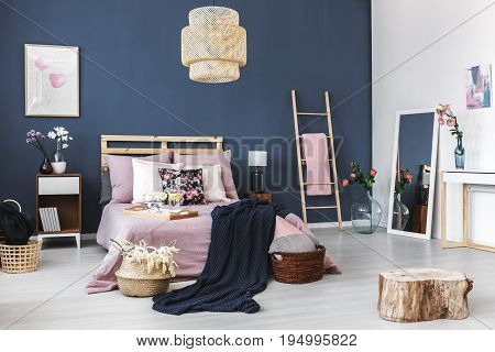 Two small wicker baskets standing next to bed with dark blanket and breakfast tray