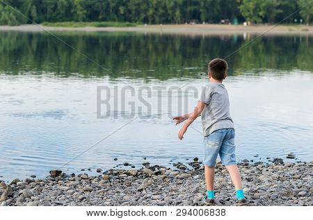 A Child, A Teenager, On A Stony Shore Throws Stones Into The River, Lake