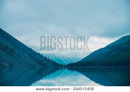 Amazing Silhouettes Of Mountains And Low Clouds Reflected On Mountain Lake. Beautiful Ripples On Wat