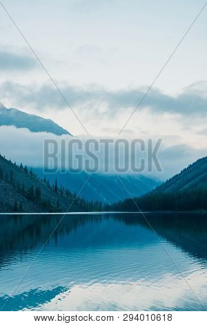 Amazing Silhouettes Of Mountains And Low Clouds Reflected On Mountain Lake. Beautiful Ripples On Wat