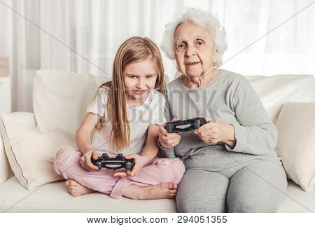 Smiling grandmother with little granddaughter playing games together with gamepads