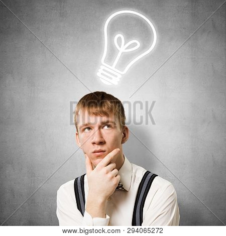 Redhead Student Thinking About Some Problem. Clever Boy On Background Of Grey Wall With Idea Lightbu