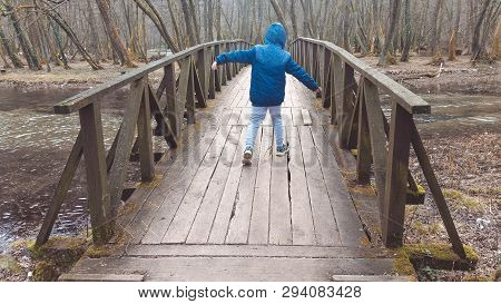 Young Boy Walking On The Wooden Bridge And Enjoying The Picturesque View Of The River.