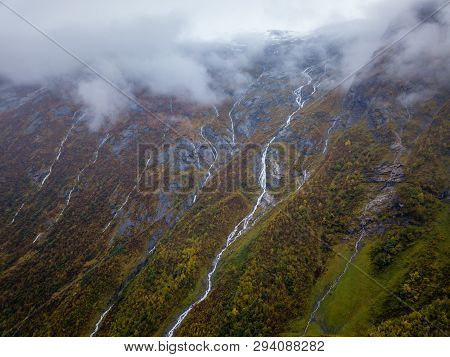 Drone Photo Of Several Small Waterfalls In Mountains With Clouds Covering Them Near Bøjabreen Glacie