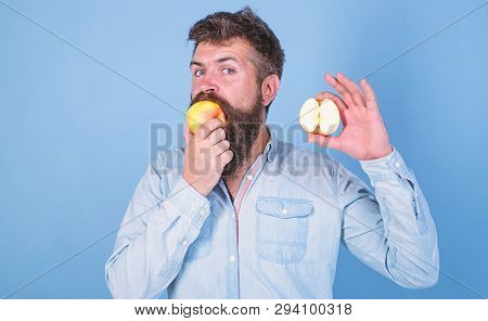 Man Bearded Eats Fruit, Holds Apple Blue Background. Half Of Apple Healthy Lifestyle. Hipster Demons