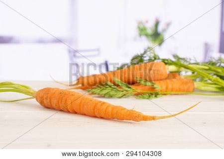 One Whole Fresh Orange Carrot In Focus With Greens With Red Flowers On White In Background