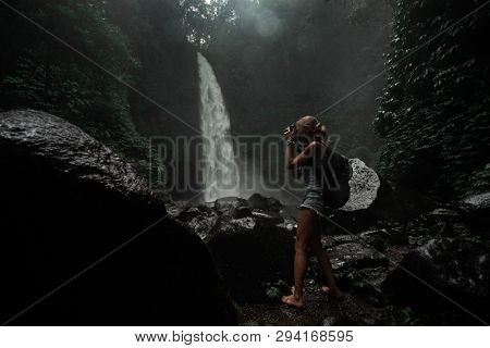 Young woman tourist taking photo of the Nung Nung waterfall, magic island of Bali, Indonesia.