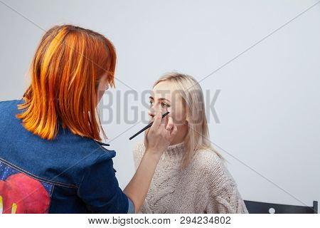 Visagiste With A Brush In One Hand Putting Makeup On The Eyes Of The Model, The Other Hand Pulls The