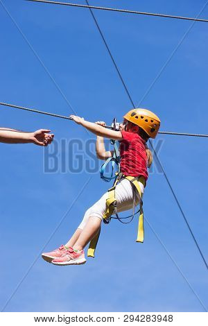 Little Brave Caucasian Girl Using A Zip Line. An Indefinited Man Lend A Helping Hand.