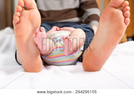 Closeup Of Huge Feet Of Father And Little Newborn Baby. Big Feet Of Adult And Tiny Legs Of Child. Ha