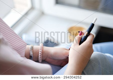 A Girl With A Manicure Holds In Her Hands A Modern Electronic Cigarette With A Heating Stick. Smokel