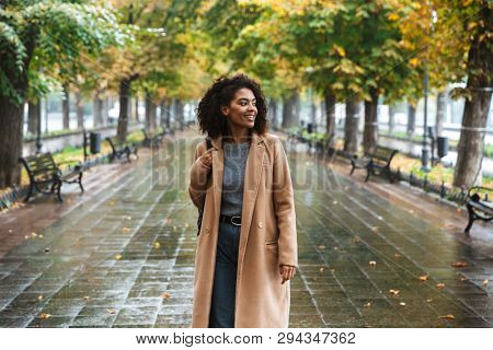 Beautiful young african woman wearing coat walking outdoors at the park, carrying backpack