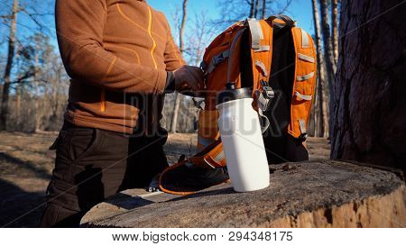 Theme Hiking And Travel. A Caucasian Tourist Man Unpacks An Orange Backpack, Takes Out His Things An