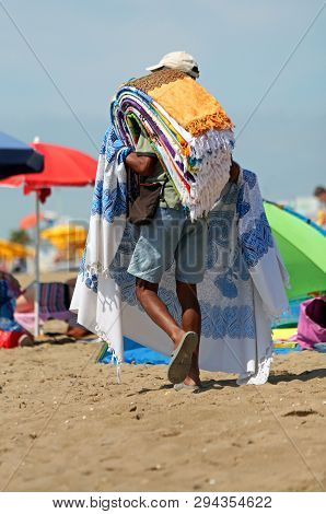 Street Carpet Vendor Walks On The Sunny Beach To Sell His Products
