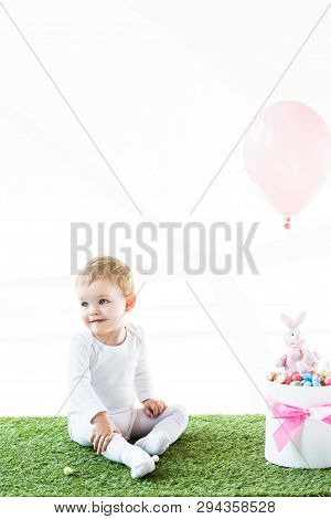 Smiling Baby Sitting Near Box With Estern Eggs, Decorative Rabbit And Air Balloon Isolated On White