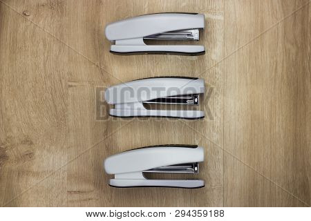 Top View On Three Office Staplers On Wooden Background.