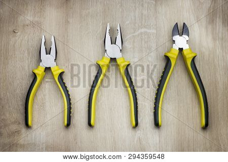 Two Yellow Combination Pliers And Side Cutters On Wooden Background.
