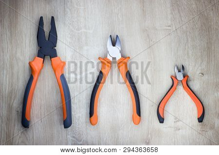 Basic Plier Set, Designed For Grasping, Bending And Cutting. Isolated On Wooden Background.