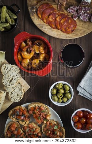 Various Tapas Dishes Cheese And Wine On A Wooden Table. Dishes Include Garlic Prawns, Toasts, Charcu