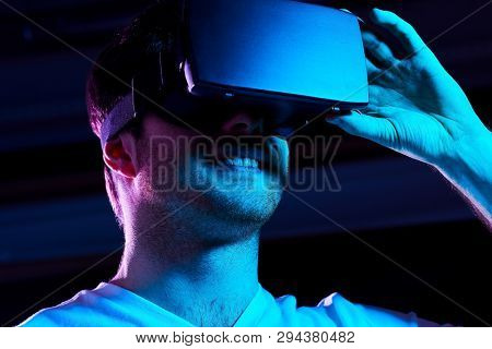 3d technology, virtual reality, entertainment and people concept - young man in vr glasses playing game over ultra violet neon lights in dark room