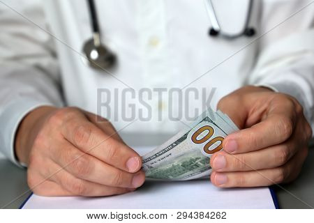 Doctor With Money, Man Sitting At The Table With Us Dollars In Hands. Concept Of Expensive Health Ca